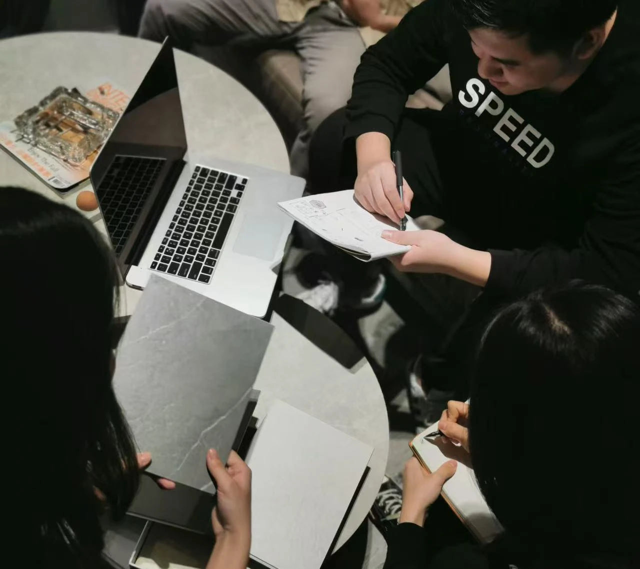 Top-down view of the Molekaus design team collaborating at a wooden workspace, discussing layout drafts and market research to create engaging, easy-to-use keepsake journals.
